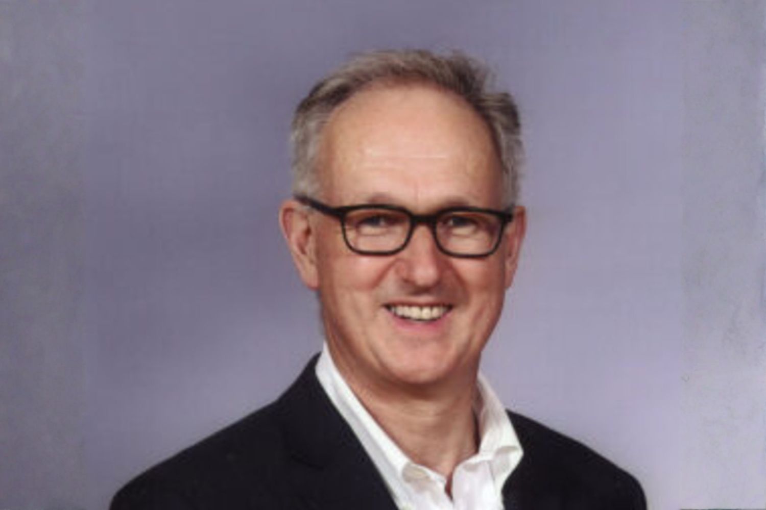 Julian Dobson of Julian Dobson Solicitors is pictured smiling, wearing glasses, and he is also wearing a black suit with a white shirt.